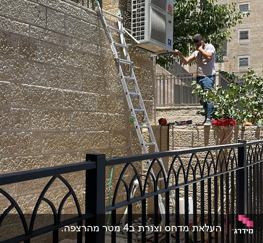 אדם עובד על מזגן על קיר חיצוני עם סולם